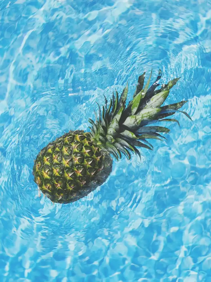 Pineapple floating in crystal clear pool water.